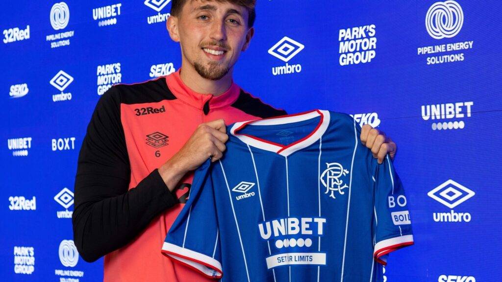 Dan Neil Rangers: Dan Neil holding up a Rangers shirt during his official signing or unveiling event.